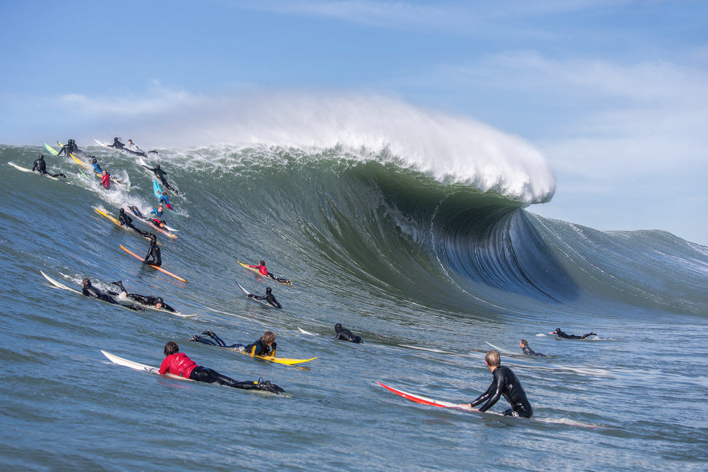 A haunting wide shot of the Mavericks lineup, where elite surfers watch a massive, unsurfable peak roll through the cold Northern California water.